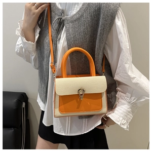 Detail of a color-block handbag with orange leather and beige textured fabric worn by model