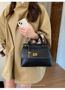 Detail of retro black faux suede bag with white contrast stitching and gold buckle