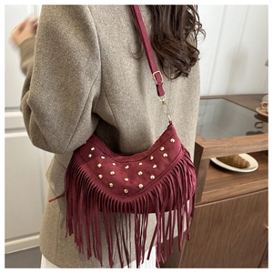 Detail of burgundy suede hobo bag with gold studs and long tassel accents in lifestyle setting