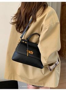 Detail of black suede satchel featuring white contrast stitching and gold twist lock closure