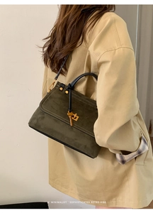 Close-up of olive green suede handbag with white stitching and metal key charm
