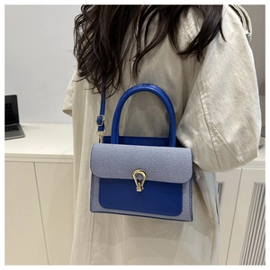 Detail of the blue contrast flap bag featuring a gold horseshoe clasp on a beige coat