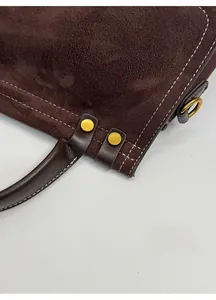 Detail of reinforced stitching and gold metal rivets on a dark brown suede handbag