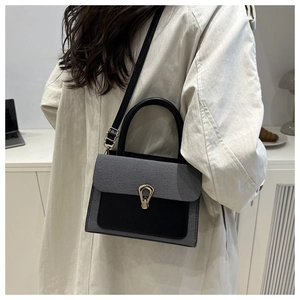 Detail of a grey twill and black leather crossbody bag with a golden horseshoe lock