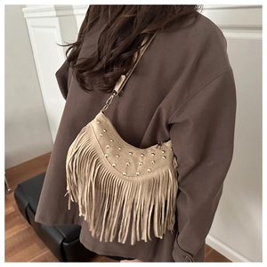 Detail of beige suede crescent bag featuring golden rivets and long fringe tassels