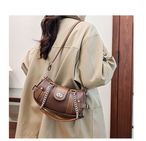 Close-up of retro brown leather handbag with metal chain on model in trench coat