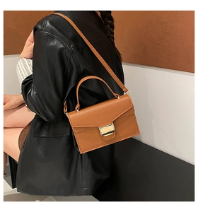 Sac à main marron texture litchi avec fermoir doré porté à l'épaule par un mannequin
