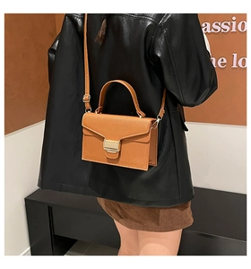 Sac bandoulière en cuir grainé marron avec boucle dorée porté par un mannequin
