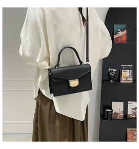 Sac à main minimaliste en cuir grainé noir avec fermoir doré porté par un mannequin