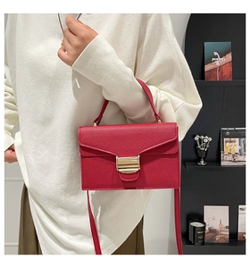 Détail d'un sac à main rouge en cuir texturé avec fermoir doré porté par un mannequin