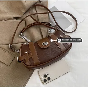 Size comparison of patchwork leather shoulder bag next to iPhone 12 on a bed