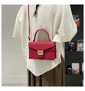 Détail d'un sac à main rouge en cuir grainé avec fermoir doré porté par un modèle