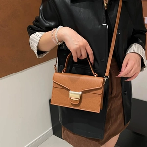 Sac à main marron texture litchi avec boucle dorée porté en bandoulière sur un mannequin