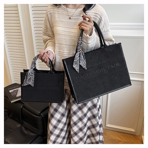 Detail of matte black tote bag set with embossed lettering and silk scarf on handles