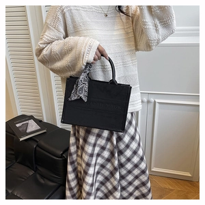 Detail of black matte tote bag featuring embossed letters and a silk scarf on handle