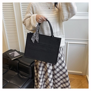 Detail of black matte tote bag with decorative silk scarf and embossed text pattern