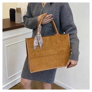 Brown suede tote bag with letter embossing and patterned scarf detail in cafe setting