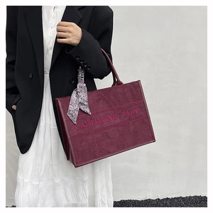Detail view of burgundy suede tote bag with printed letters and elegant silk scarf handle