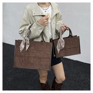 Detail of two brown suede tote bags with embossed text and silk scarves on handles