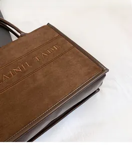 Detail of dark brown suede tote bag with signature embroidery and leather trim