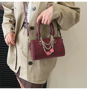 Close-up of burgundy Boston bag with gold chain and detailed strawberry charms