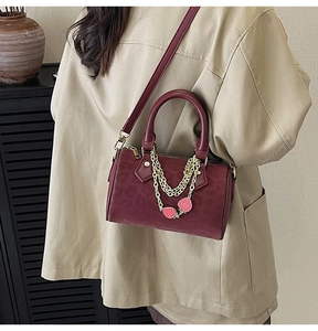 Detail of burgundy leopard embossed boston bag with gold chains and strawberry charms