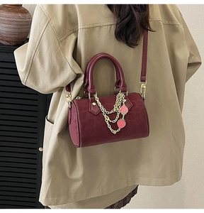Detail of burgundy Boston bag with gold strawberry chain and leather crossbody strap