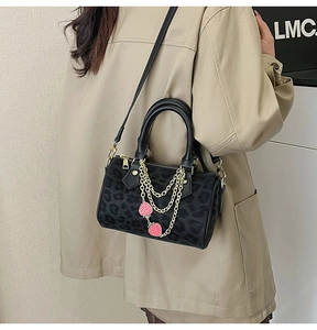 Detail view of leopard print Boston bag with gold chain and strawberry charm on trench coat
