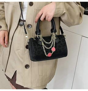 Detail of black leopard embossed handbag featuring gold chains and strawberry charms