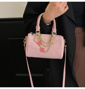 Pink boston bag with gold chain and strawberry charms held by woman in black coat