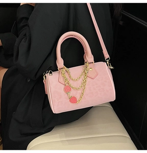 Close-up of pink mini Boston bag with gold strawberry chains and crossbody strap detail