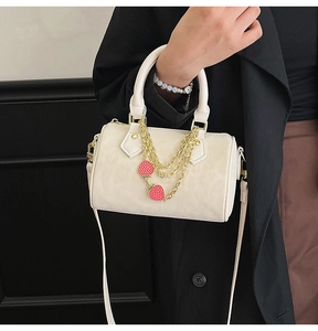 Detail view of cream Boston bag featuring gold hardware and a strawberry charm chain