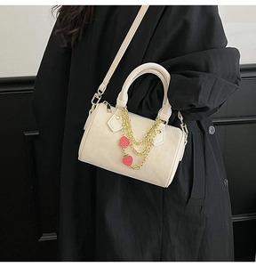 Close-up of cream Boston bag with gold chain and red strawberry pendants on black coat