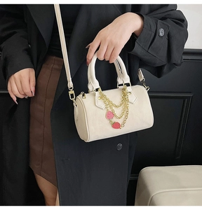 Detail of cream Boston bag with gold chains and red strawberry charms in hand