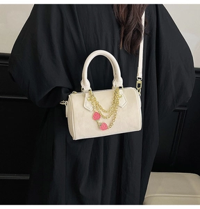 Detail of cream Boston bag with gold chains and strawberry charms held by a model