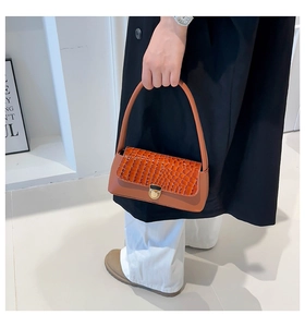 Detail of crocodile embossed orange baguette bag with round gold lock and smooth strap