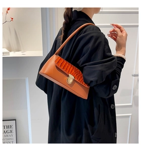 Detail of orange faux-leather underarm bag with crocodile pattern flap and gold clasp