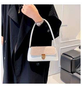 Detail of white baguette bag with crocodile pattern flap and gold clasp on black coat