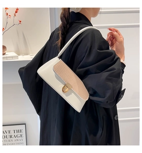 Detail of white baguette bag with snakeskin flap and golden metal lock on black coat