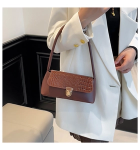 Detail of a brown crocodile pattern shoulder bag with a gold clasp on a model