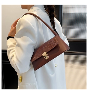 Detail of a brown crocodile texture baguette bag with a gold metal clasp on a model