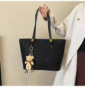 Detail of vintage leopard print tote bag with a plush bear charm on a beige coat background
