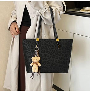 Close-up of vintage leopard print tote bag with plush bear charm and golden hardware