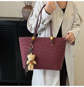 Detail of burgundy leopard embossed tote bag with gold metal buckles and plush bear charm