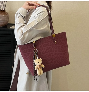 Detail of burgundy leopard print tote bag featuring a cute plush bear pendant accessory