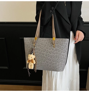 Detail of gray leopard print tote bag with plush bear charm and striped silk scarf