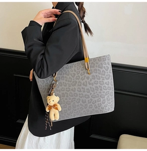 Side view of leopard print tote bag with brown handles and plush bear charm on model