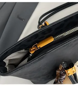Detail of smooth gold zipper and leopard texture on black leather tote bag