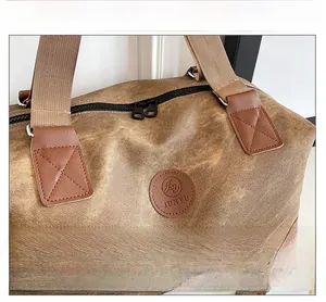 Macro view of brown canvas travel bag showing double zipper and leather logo detail