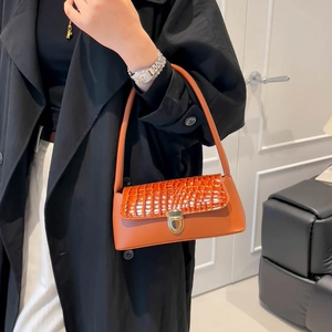 Orange baguette shoulder bag with crocodile texture flap and gold buckle on a model